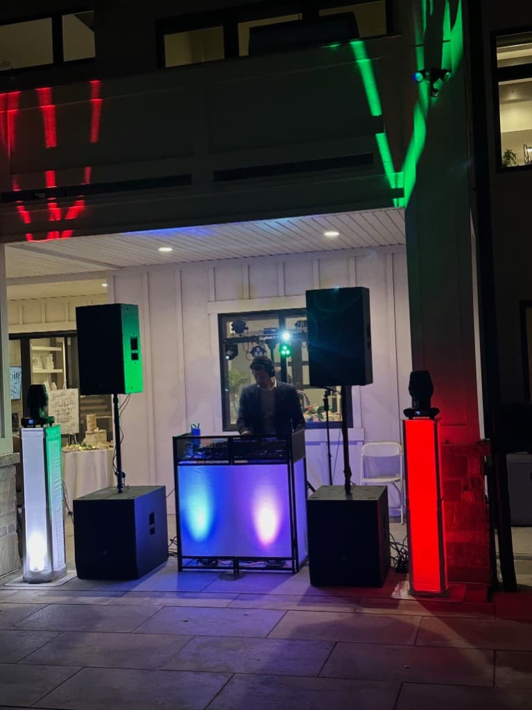 Outdoor DJ booth at night with speakers and colored event lighting